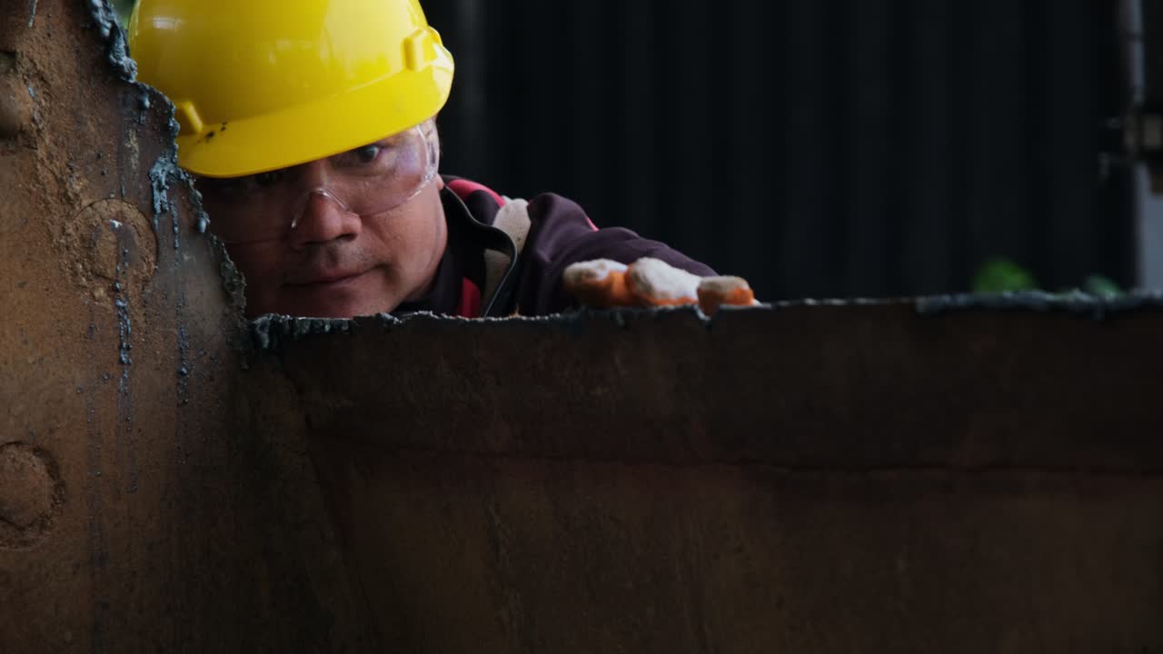 trabajador masculino con gafas de protección y guantes de construcción inspecciona el trabajo después de moler metal con un molinillo angular en el taller doméstico.