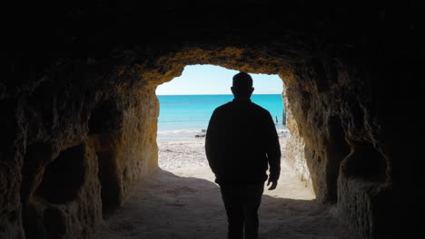 a man looking out of a tunnel towards the beach and ocean during the day