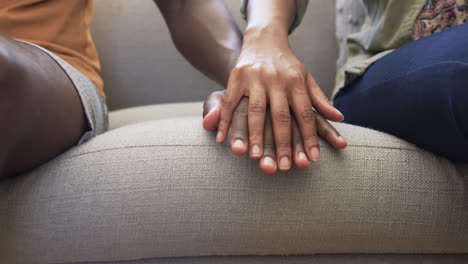 pareja diversa sentada cerca, manos tocándose en el sofá