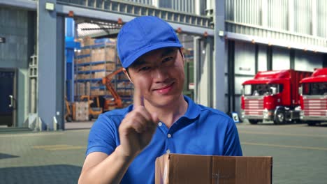 close up of asian male courier in blue uniform showing no gesture while delivering a carton, outside of logistics distributions warehouse