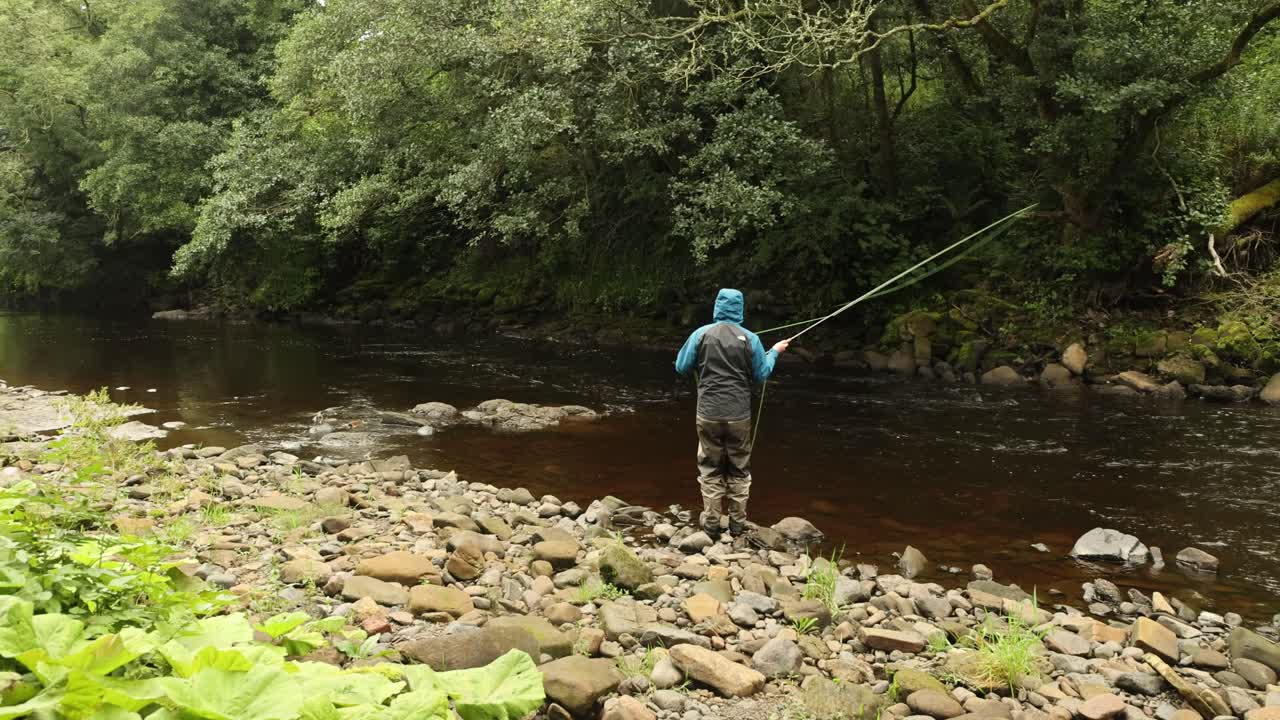 Plano cámara en mano de un pescador con mosca lanzando en una sección de río de caudal rápido.