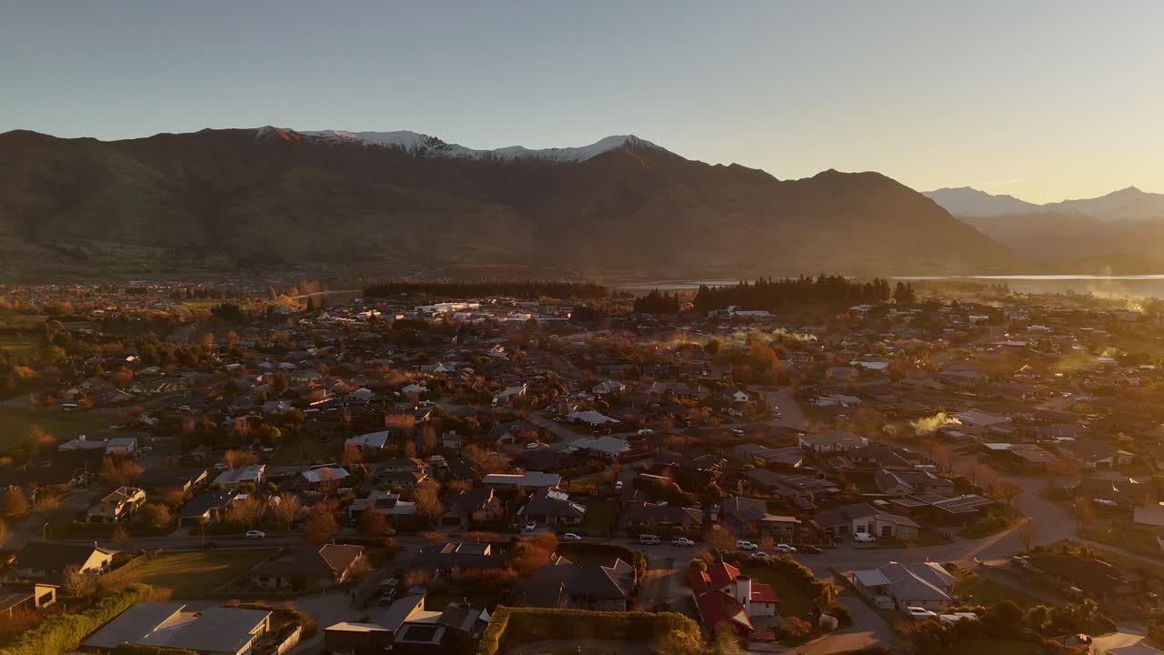 Forward-moving aerial of Wanaka town in New Zealand during a hazy winter morning at golden hour