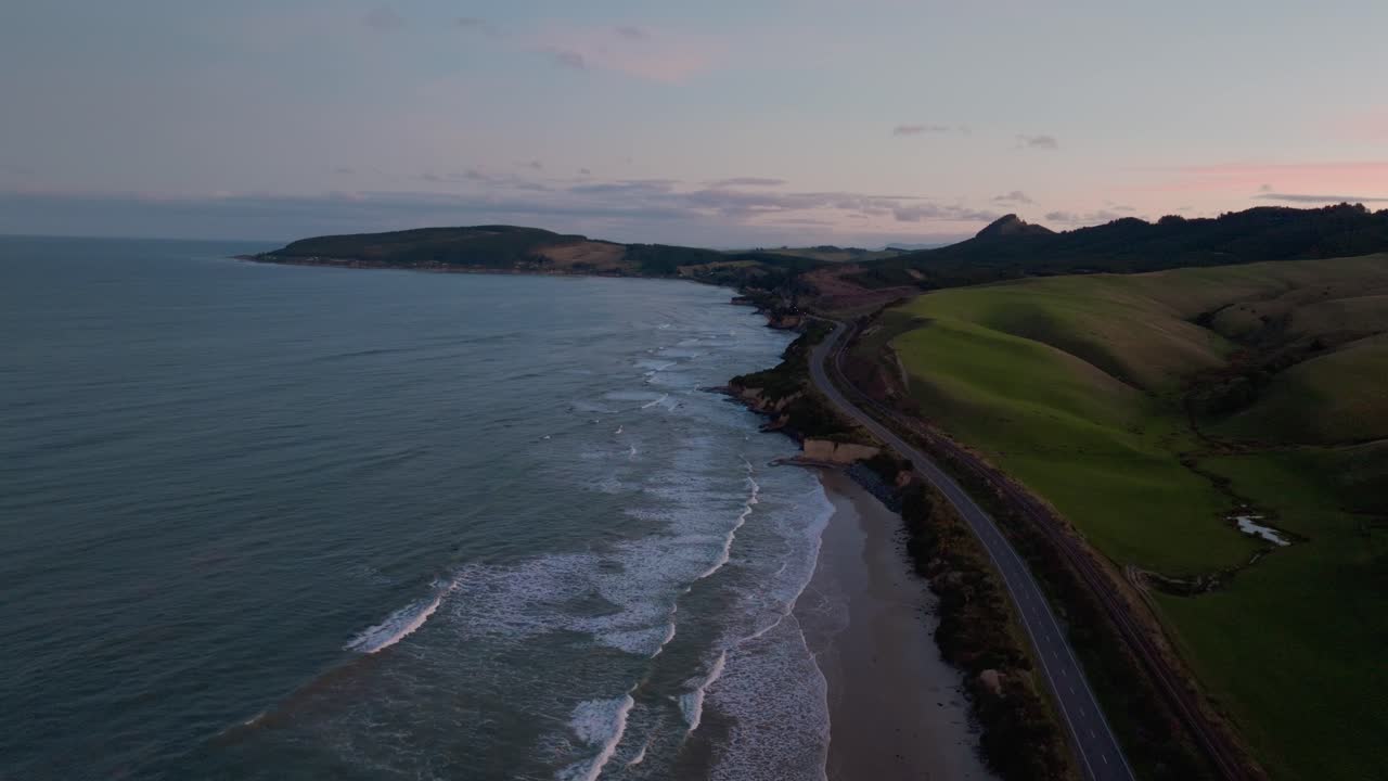 vuelo aéreo sobre el océano tranquilo y plácido con olas rodantes que calientan el resplandor en el cielo en la península de katiki en el norte de otago, nueva zelanda aotearoa