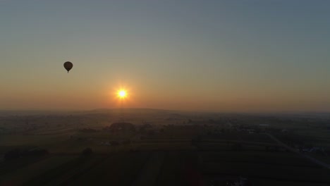 amanecer de un globo aerostático en una mañana nublada sobre tierras de cultivo amish visto por un dron