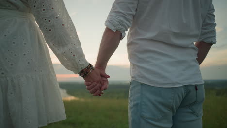 a close-up of lovers holding hands gently, with the woman s hand adorned with beaded bracelets and red nails. the soft sunlight illuminates the scene, creating a warm and intimate atmosphere