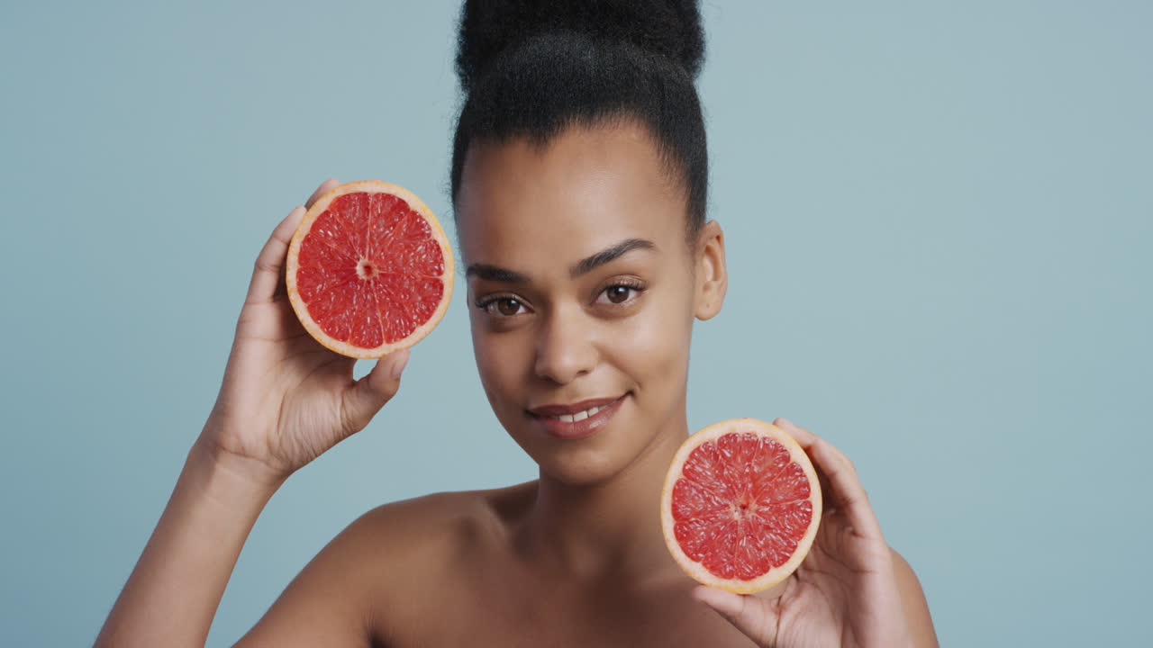 ritratto attraente giovane donna afroamericana che tiene in mano un pompelmo sorridendo godendo di un'essenza naturale di cura della pelle sana donna bella con una carnagione perfetta sullo sfondo blu