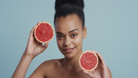 Porträt-Einer-Attraktiven-Jungen-Afroamerikanerin-Mit-Grapefruit,-Die-Lächelnd-Die-Natürliche,-Gesunde-Hautpflegeessenz-Genießt.-Schöne-Frau-Mit-Perfektem-Teint-Auf-Blauem-Hintergrund