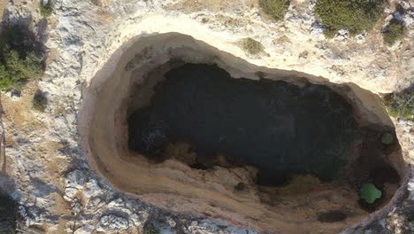 fontainhas beach in south portugal with eroded sea cave pit, aerial top view dolly up