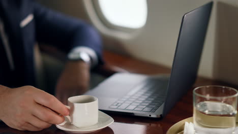 relaxed businessman working computer on trip. closeup hand putting coffee cup