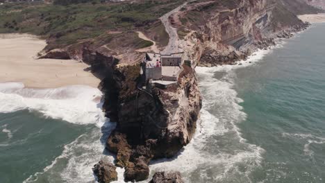 Vista-Aérea-De-ángulo-Alto-De-La-Fortaleza-En-Lo-Alto-De-Un-Acantilado-De-San-Miguel-Arcángel-Y-El-Faro-De-Nazare