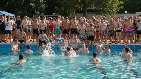 a summer pool party scene: a large crowd of people cheers as participants engage in water fun, diving, and excitement amidst sunny weather and vibrant atmosphere