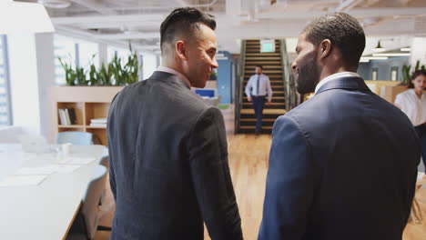 two businessmen meeting and shaking hands in modern open plan office