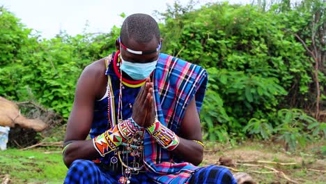 Masked-African-person,-praying-for-the-victims-of-the-Covid-19-pandemic,-wearing-traditional-clothing