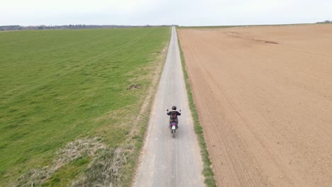 drone actively tracking an accelerating motorcycle rider along an empty gravel road in the european countryside