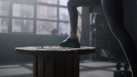 Athlete-feet-jumping-on-wooden-box.-Woman-training-legs-in-sport-club