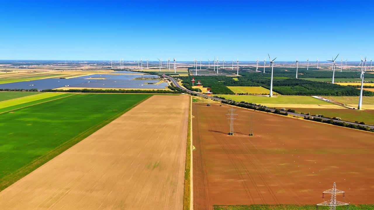 Flying over the brown field with electric supports. Wind turbines located in the plantation at backdrop