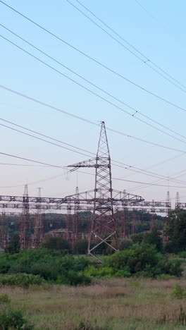 lots of electricity towers on field. large power station with many high-voltage electric lines with wires against the sky background. transmission lines in green nature. vertical video