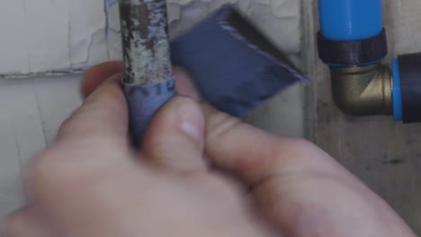 A-man-uses-sandpaper-on-an-old-copper-pipe-before-soldering