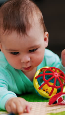 caucasian little kid lies on belly on a mat. baby boy in blue clothes plays with toys. close up. vertical video