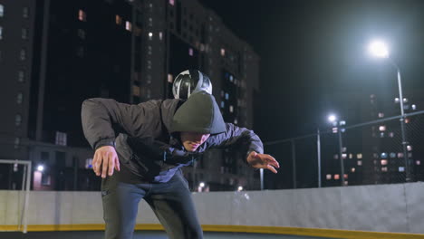 el deportista lanza hábilmente la pelota, la equilibra en la espalda, la empuja hacia arriba y la atrapa durante la práctica nocturna en un campo rodeado de edificios residenciales iluminados y farolas brillantes