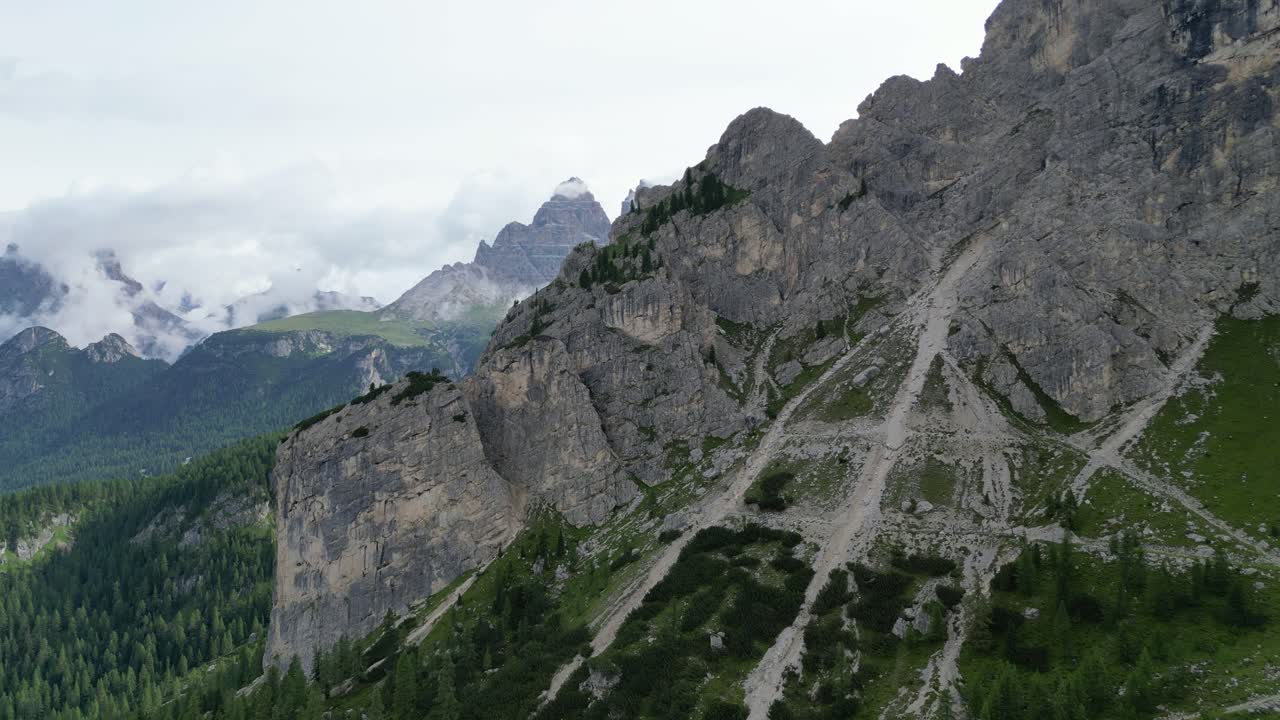 Dolomite peaks rise dramatically, partially veiled by clouds with steep and rocky slopes. Dolomites, Italy