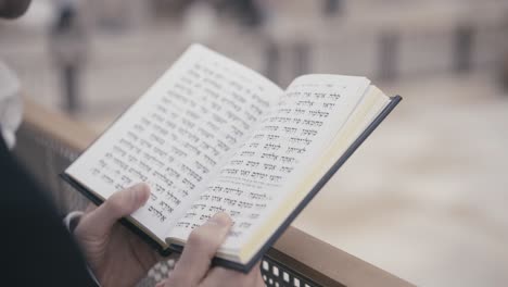 jewish man praying. he holds a prayer book with hebrew writing in his hands. its a close up shot with a background of the western wall in jerusalem, israel. action is in slow-motion.
