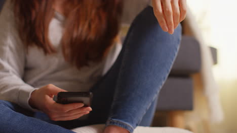 close up on hand of woman sitting on sofa at home using mobile phone to check social media message and scrolling online 2