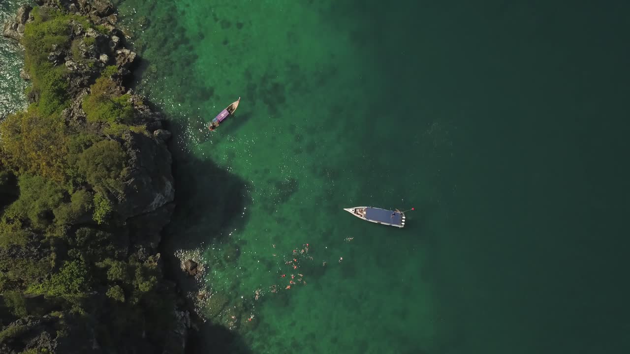 Ascending Top Aerial View of Boats and People Snorkeling in Tropical Sea by Rocky Cliff Islet, Krabi Thailand