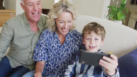 Glückliche-Kaukasische-Großeltern-Mit-Enkel,-Der-Selfie-Macht-Und-Im-Wohnzimmer-Sitzt