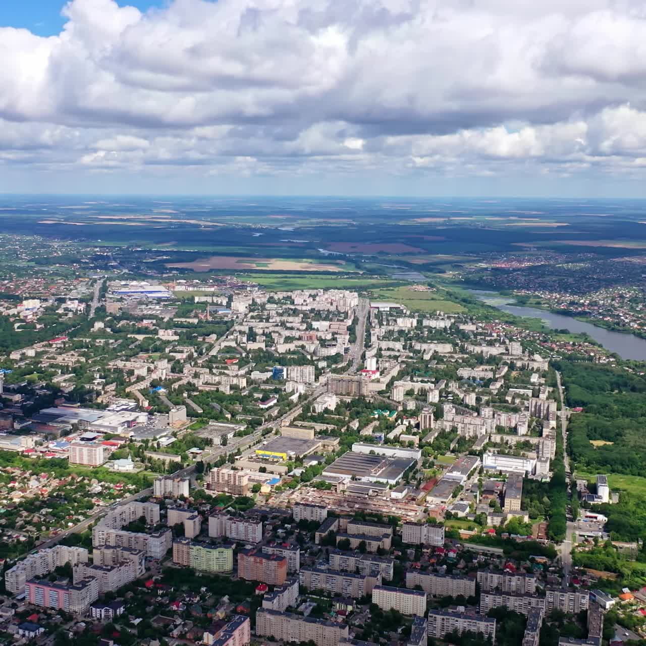 Cityscape under blue clouds. Beautiful view on the city surrounded by nature. Aerial view. Camera rising up.