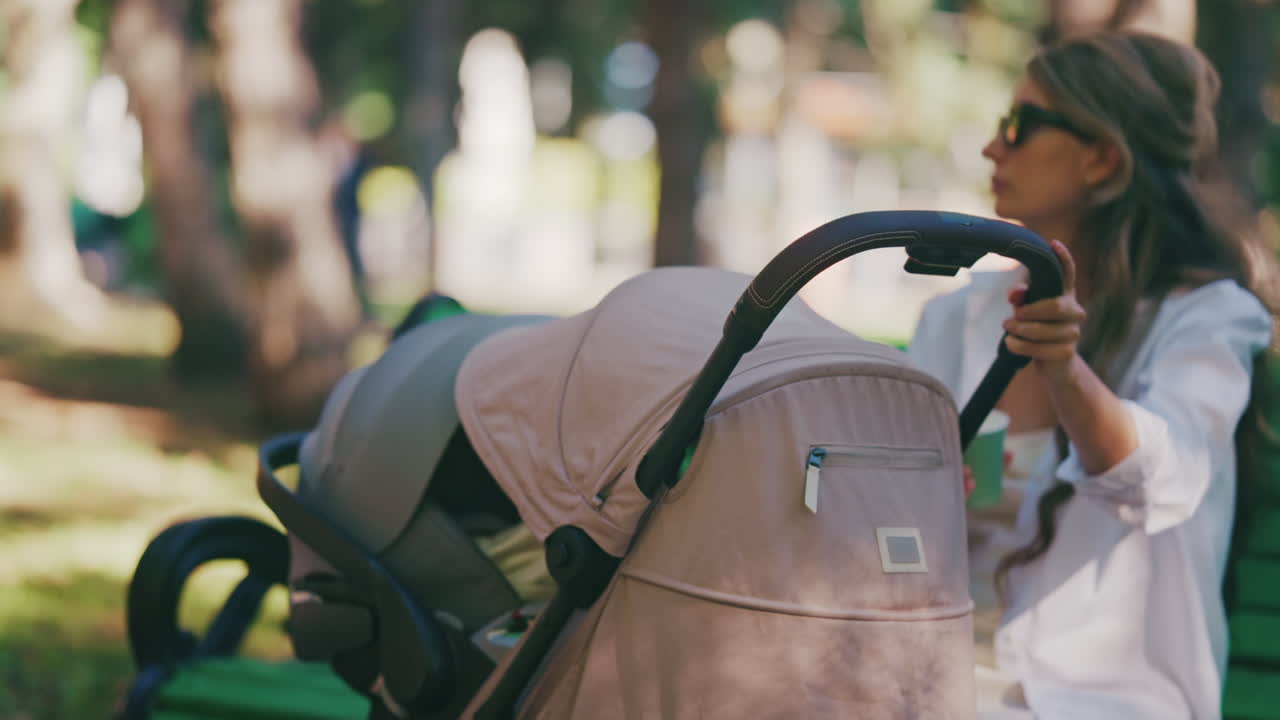 Young mother sitting on a park bench next to a stroller, enjoying a peaceful outdoor moment with her baby