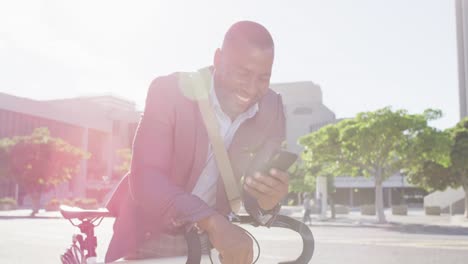 african american man in city, sitting on bike in the sun using smartphone