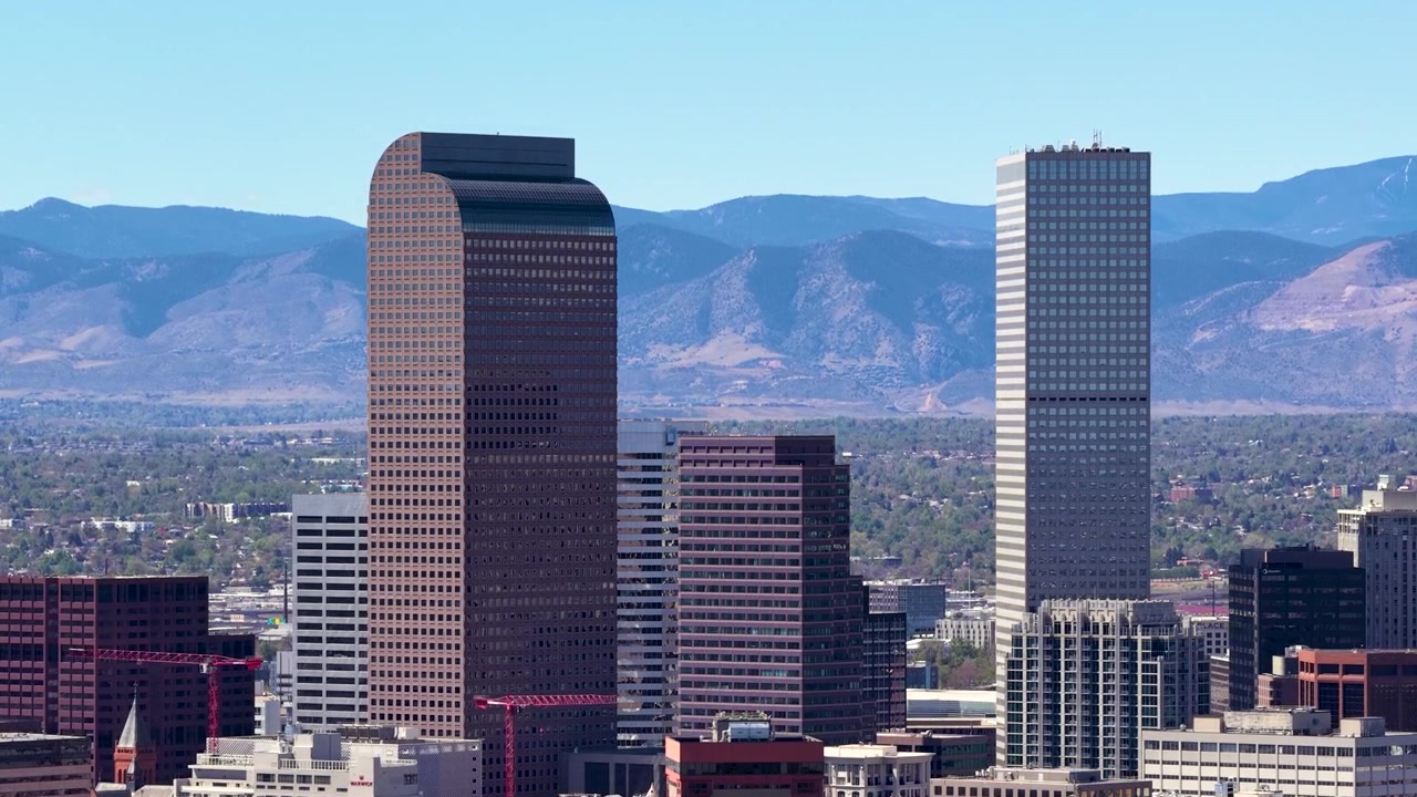 Veduta aerea con drone del caratteristico Cash Register Building con la cima ad arco tra i grattacieli di Denver e le montagne sullo sfondo.