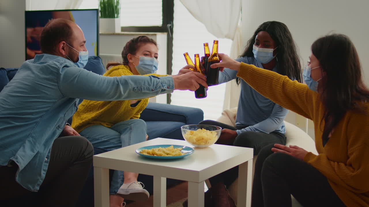 Happy diverse people having fun in living room, clinking bottles of beer