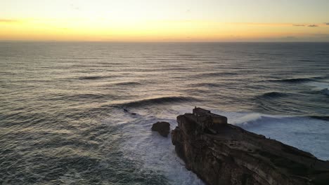 golden sunset over the waves and rocky coastline with a lighthouse in portugal
