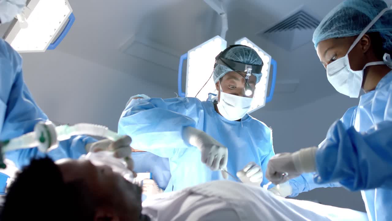Diversi chirurghi che indossano camici chirurgici operano un paziente in sala operatoria, al rallentatore.