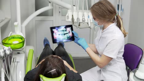 female doctor dentist is showing x-ray teeth on tablet to young female patient. dentist is wearing lab coat