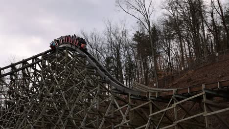 slow motion view of rollercoaster going through banked curve and coming to a stop with riders in red cars on cloudy afternoon. lightning rod coaster at dollywood with visitors getting thrill.