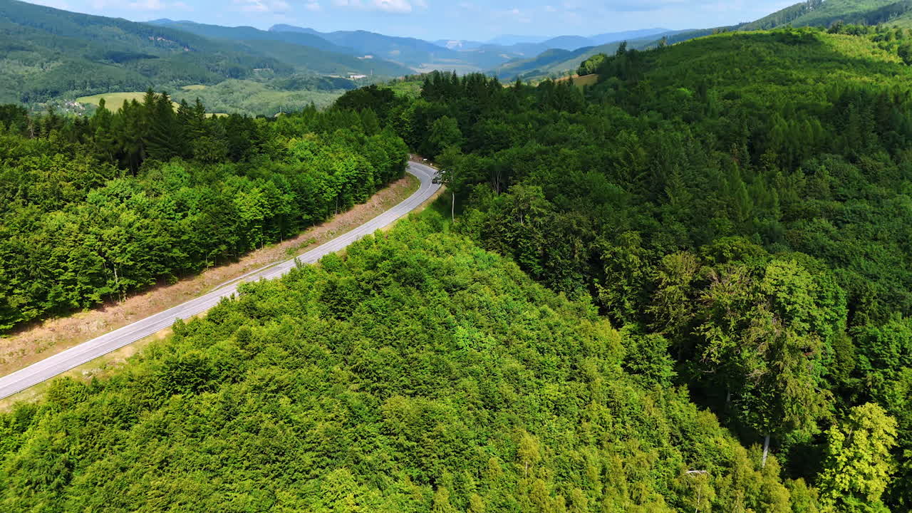 Winding mountain road through forest. A winding road cuts through vibrant green hills, surrounded by dense forests under a clear blue sky
