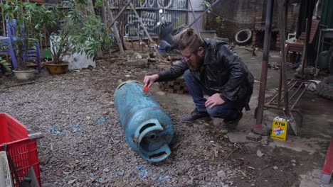 man cleaning and removing flaking paint, blue gas storage cylinder