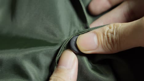 fingers pressing attaching snap button of green jacket, close up