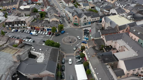 Aerial-ascending-footage-of-traffic-on-roundabout-in-town-centre.-Cars-parked-along-road-in-front-of-buildings-around-square.-Ennis,-Ireland