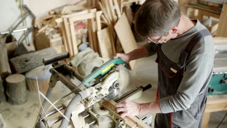 high angle view of mature furniture maker using circular saw to make cuts in wooden plank in his workshop