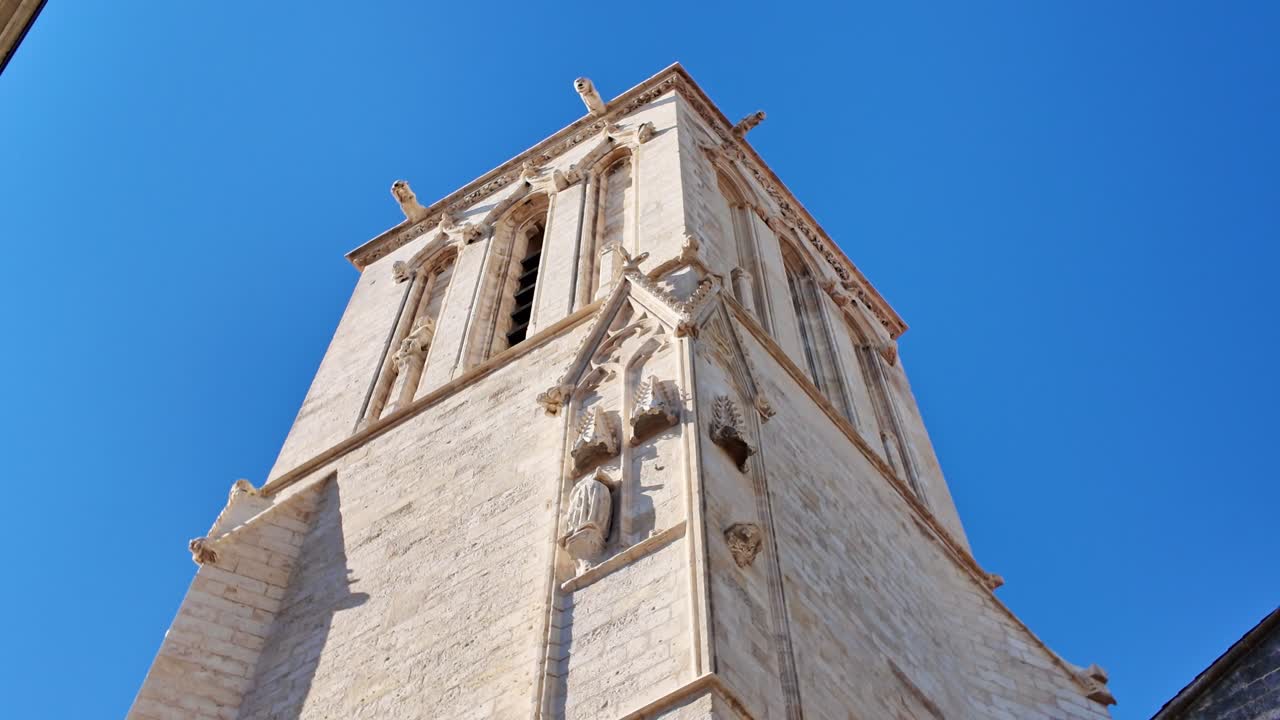 Camera tilts upward along Saint-Sauveur Church in La Rochelle, showing stone walls and stained glass windows- France