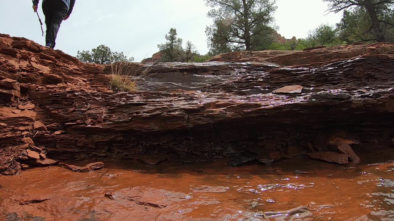 A hiker makes his way along the trickle of spring runoff down the sandstone steps, Sedona, Arizona.