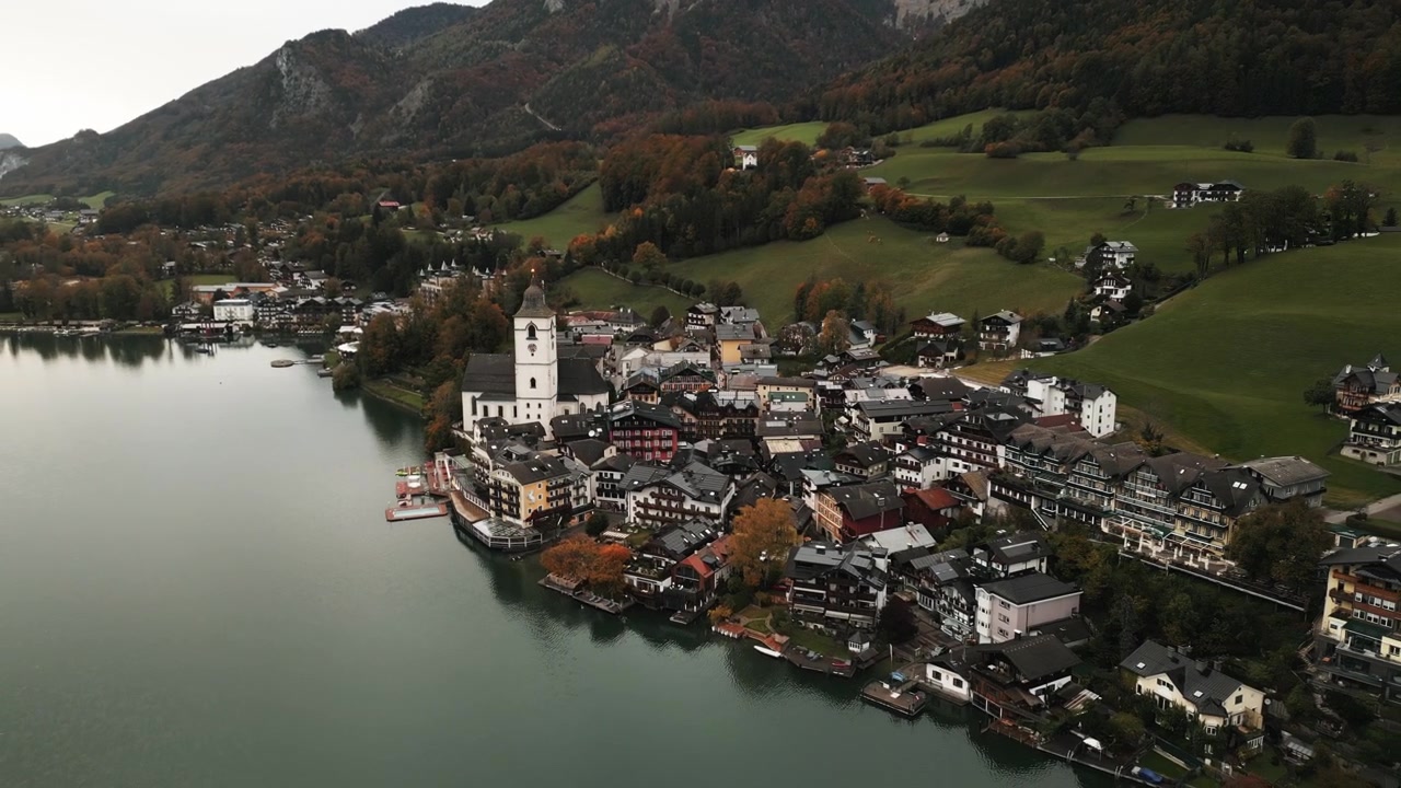 Bevægelig luftdroneoptagelse af Wolfgang am Wolfgangsee langvejsfra på en overskyet dag tæt på søen.