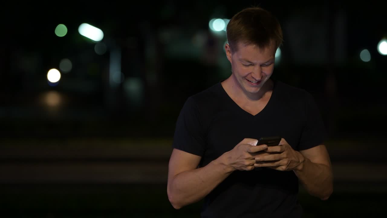 젊은 잘생긴 스칸디나비아 남자가 밤에 거리에서 전화를 사용합니다.