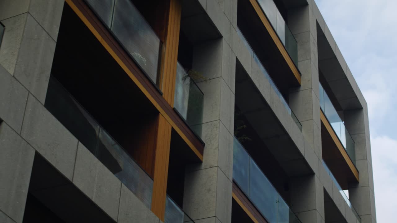 Low-angle shot of a modern apartment complex with sleek concrete and wood finishes, large glass balconies, and minimalist design, highlighting urban luxury real estate