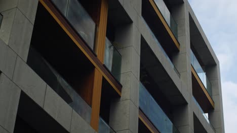 low-angle shot of a modern apartment complex with sleek concrete and wood finishes, large glass balconies, and minimalist design, highlighting urban luxury real estate