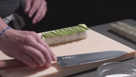 a roaming shot captures a sushi chef placing fresh avocado slices onto a sushi roll, showcasing the precision and artistry of sushi preparation. ideal for culinary and sushi-making content.